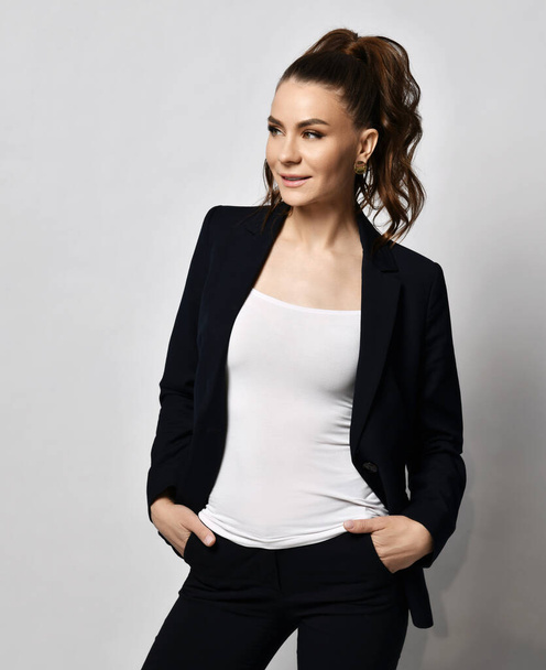 Young smiling brunette businesswoman in black official suit standing and looking away - Photo, Image