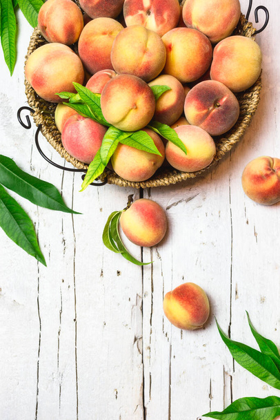 Спелые красные персики в корзине на деревенском белом столе, вид сверху. Здоровые органические фрукты. - Фото, изображение
