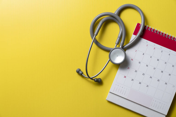 Top view of stethoscope and calendar on the yellow background, schedule to check up healthy concept - Fotografie, Obrázek
