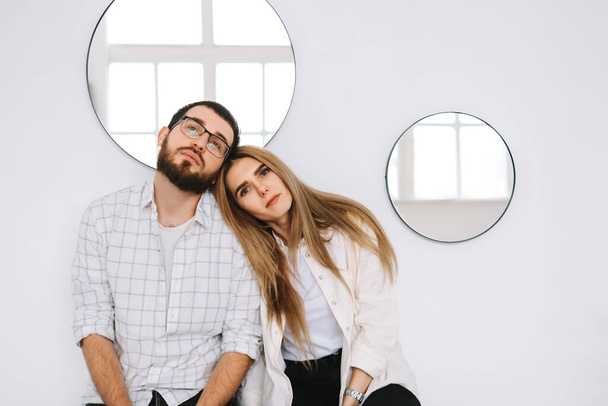 Porträt eines glücklichen Paares, das zu Hause auf dem Sofa in der Nähe der weißen Wand sitzt und in die Kamera blickt. - Foto, Bild