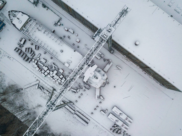 Een kraan op een met sneeuw bedekte scheepswerf. Sneeuwdag, sneeuwstorm. Luchtdrone zicht. - Foto, afbeelding