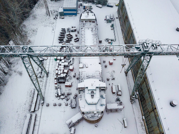 Żuraw w stoczni pokrytej śniegiem. Śnieżny dzień, śnieżyca. Widok drona z powietrza. - Zdjęcie, obraz