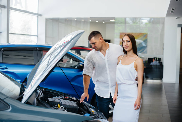 A young couple chooses a new car at the dealership and consults with a representative of the dealership. Used cars for sale. Dream fulfillment - Foto, afbeelding