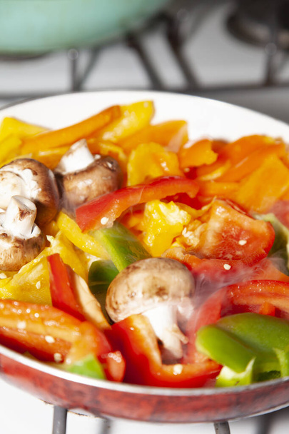 Sliced red, yellow, orange, and green bell peppers and whole portabella mushrooms in a frying pan - Valokuva, kuva
