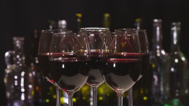Rode wijn. Elegante wijnglazen met rode wijn op de achtergrond van een rij alcoholflessen. Langzame rotatie - Video