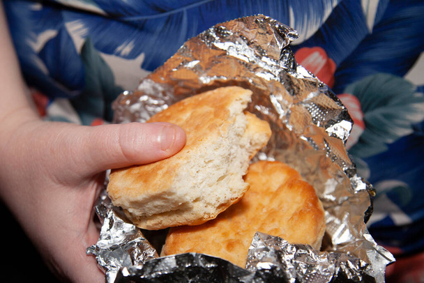 Woman's hands holding two buttermilk biscuits, one of which has been partially eaten, in foil - Photo, Image