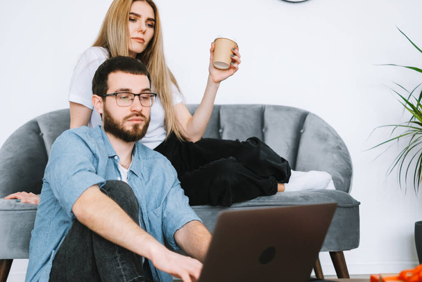 Young couple using laptop computer and resting on the sofa at home together. High quality photo - Fotó, kép