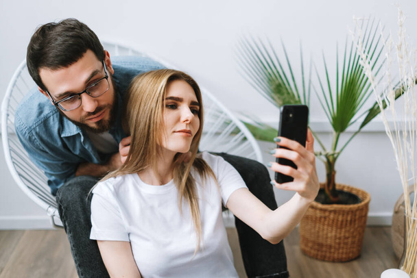 Young cheerful couple using mobile phone, making selfie on smartphone together. High quality photo - Foto, imagen