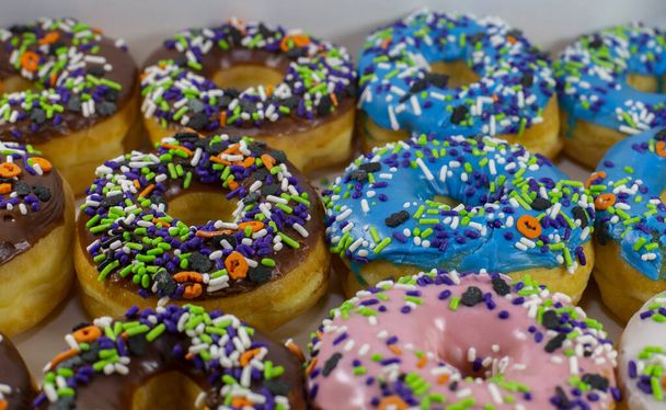 Donuts met bruine, blauwe, roze en witte glazuur bedekt met veelkleurige hagelslag in een witte doos - Foto, afbeelding