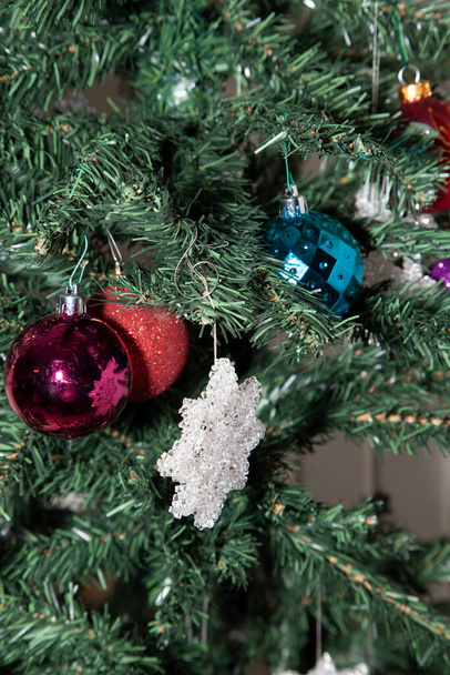 Globos púrpura, rojo brillante y azul cerca de una decoración de estrellas claras en un árbol de Navidad artificial - Foto, Imagen