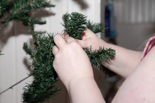Mujer dando forma a las extremidades de un árbol de Navidad verde artificial - Foto, imagen
