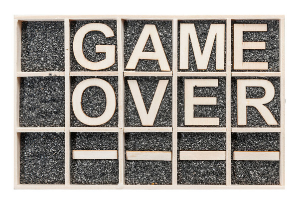 Ve sběrné krabici s černým dekorativním pískem uspořádané překližky písmena slovo GAME OVER naskládané v horní pohled na bílém pozadí. - Fotografie, Obrázek