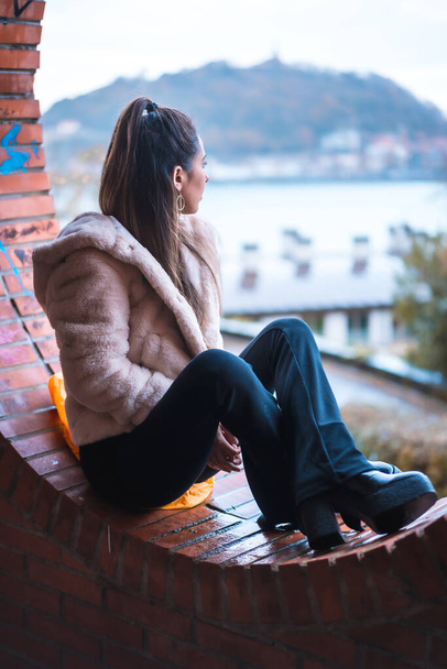 Caucasian brunette model sitting in winter looking at the city. Street style fashion - Foto, immagini