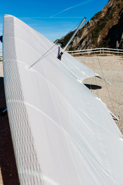 Ευρεία γωνία θέασης με χαμηλά βάθη του πεδίου πάνω από την φέρουσα επιφάνεια ενός λευκού αετό ανεμόπτερο κατά ένα καλοκαιρινό μπλε ουρανό στο Tegelberg στη Βαυαρία. Η εστίαση είναι στα καλώδια τάσης.. - Φωτογραφία, εικόνα