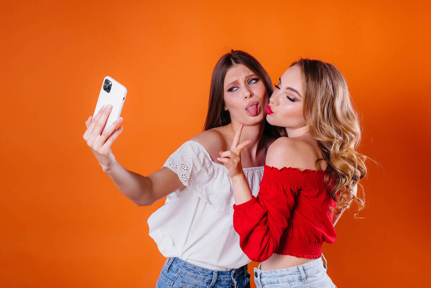 Two young and beautiful girls take a selfie and watch the phone in the Studio on a purple background. Girls for advertising - Foto, Imagem