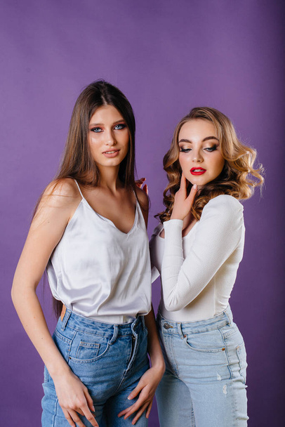 Two young and beautiful girls shows emotions and smiles in the Studio on a purple background. Girls for advertising - Φωτογραφία, εικόνα