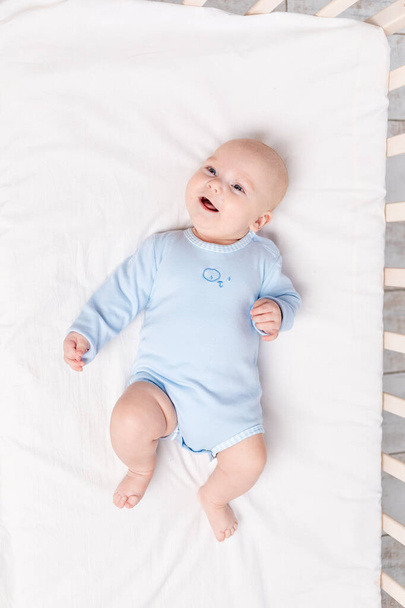 幸せな赤ちゃんはベッドの上の保育園に6ヶ月のかわいい男の子が横たわっています - 写真・画像