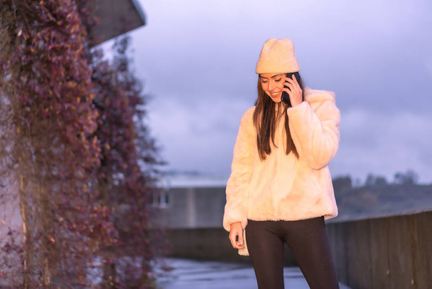 Young pretty Caucasian brunette in the city making a call with the phone, wearing a pink wool sweater and hat. Street style fashion - Fotoğraf, Görsel