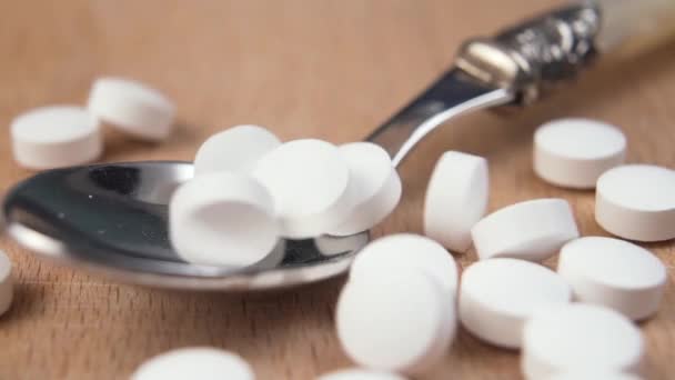 Bílé vitaminové tablety padají ve zpomaleném pohybu do lesklé kovové lžíce na dřevěném povrchu. Makro. Dolly shot - Záběry, video