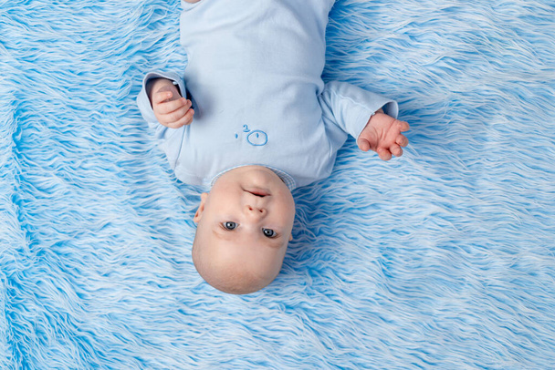 el bebé se acuesta en la alfombra azul de la casa y mira a la cámara - Foto, imagen