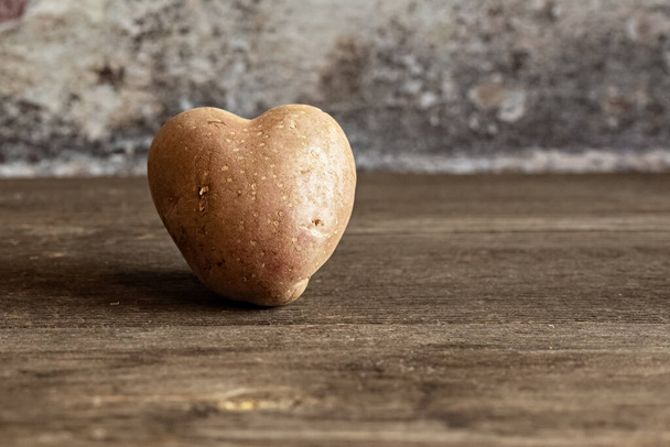 Hartvormige rode aardappel op vintage achtergrond.Het concept van landbouw, oogsten, vegetarisme. Valentijnsdag. vierkant, lelijk eten - Foto, afbeelding
