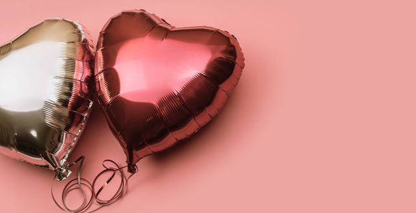Dos globos de papel de aluminio en forma de corazón sobre un fondo rosa con lugar para el texto. Globos rojos y plateados sobre fondo claro. - Foto, imagen