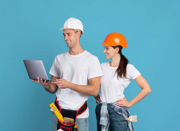 Happy young couple in hardhats using laptop, ordering materials for repair apartment - Photo, Image