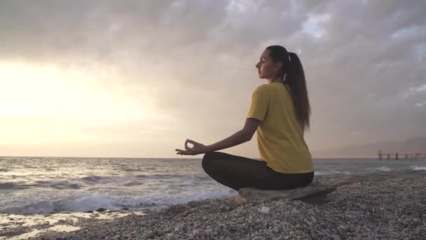 Lótuszpozícióban lévő jógás nő jógázik és meditál. szabadban az esti óceánon - Felvétel, videó