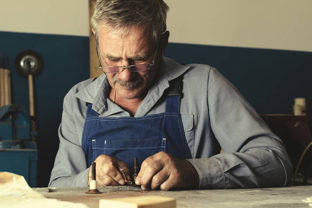 Старый мастер в очках работает в мастерской - Фото, изображение