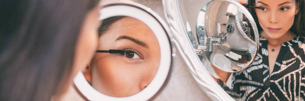 Personal beauty LED lighted round makeup mirror Asian woman putting mascara make-up at home bathroom morning routine panoramic banner. Beautiful girl getting ready. Closeup on eye in reflection - Foto, Bild