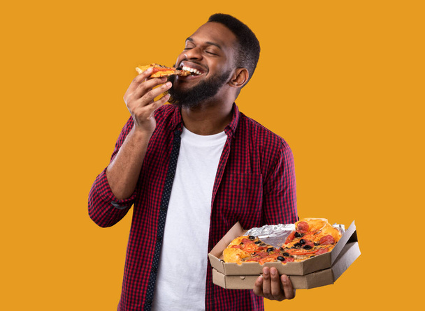 African Young Man Enjoying Pizza Posing With Box, Yellow Background - Photo, Image