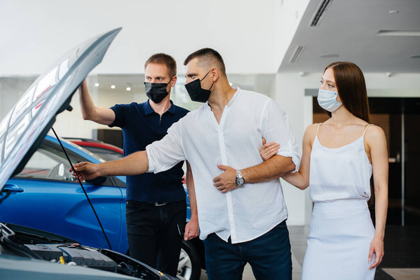 Young couple in masks selects a new vehicle and consult with a representative of the dealership in the period of the pandemic. Car sales, and life during the pandemic - Φωτογραφία, εικόνα