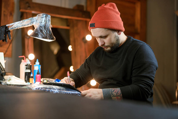Professional male bearded caucasian tattoo master is working in cozy atmospheric studio - Photo, Image