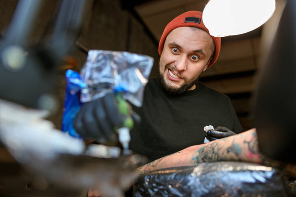Profesionální muž vousatý kavkazský tetovací mistr pracuje v útulném atmosférickém studiu - Fotografie, Obrázek
