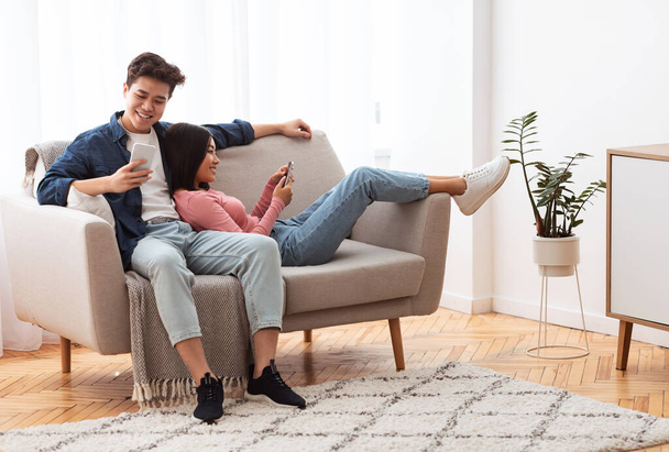 Chińska para przy użyciu telefonów Relaks siedzi na kanapie w domu - Zdjęcie, obraz