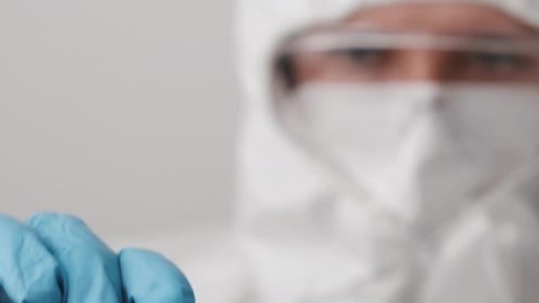 Lekarz w kombinezonie ochronnym, masce do twarzy, googlach ochronnych i gumowych rękawiczkach demonstruje szczepionkę przeciwko koronawirusowi. Opracowanie i testowanie szczepionki Covid 19 - Materiał filmowy, wideo