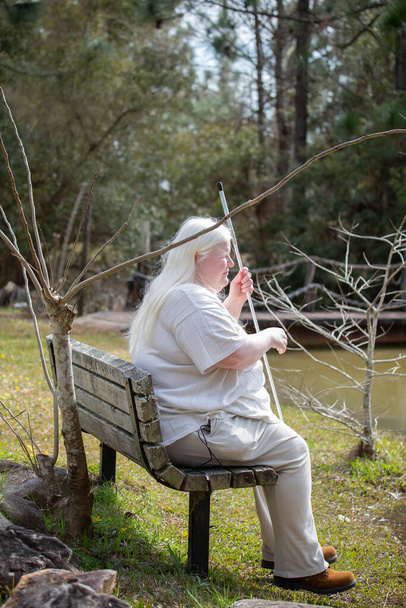 Femme aveugle assise sur un banc près d'un étang - Photo, image