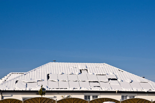 Σύγχρονα μαύρα ηλιακά πάνελ στην οροφή ενός σπιτιού το χειμώνα, καλυμμένα με χιόνι. Πράσινη ενέργεια εκτός εποχής έννοια - Φωτογραφία, εικόνα