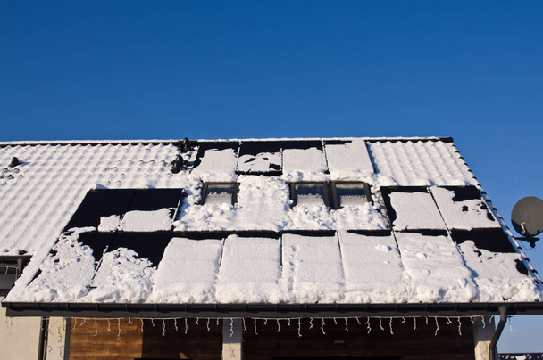 Paneles solares negros modernos en el techo de una casa en invierno, cubiertos de nieve. Energía verde fuera de temporada concepto - Foto, Imagen