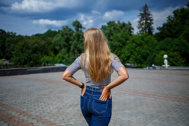 Ein schönes Mädchen mit blonden langen Haaren von europäischem Aussehen. Bekleidet mit Jeans und T-Shirt. Spaziergang an einem sonnigen Tag - Foto, Bild