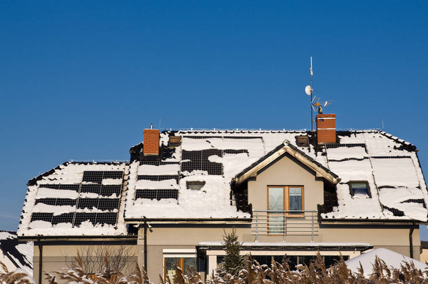 Moderní černé solární panely na střeše domu v zimě, pokryté sněhem. Koncept zelené energie mimo sezónu - Fotografie, Obrázek