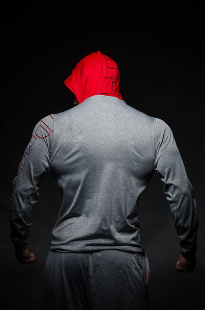 A sporty guy stands in the Studio against a dark background in a hood. Sports, beauty - Photo, Image