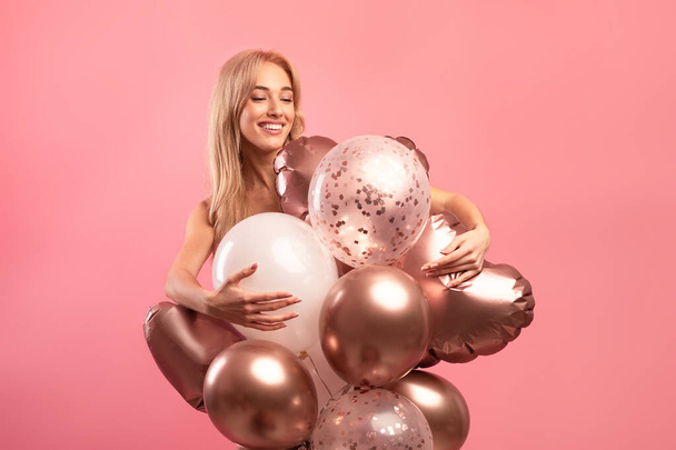 Graceful blonde birthday lady posing with colorful balloons over pink studio background - 写真・画像