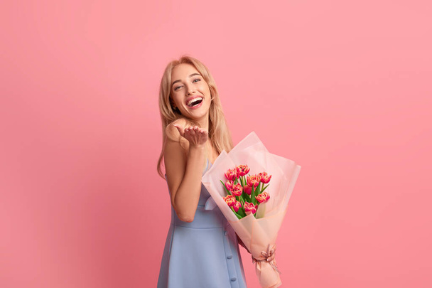 Wesoła młoda dama z pięknymi wiosennymi kwiatami śmiejąc się i patrząc na aparat fotograficzny na różowym tle studio - Zdjęcie, obraz