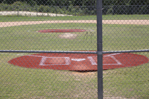 Thuisplaat van een leeg honkbalveld door een hek - Foto, afbeelding