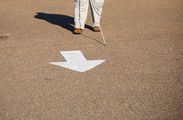 Sokea nainen, jolla on keppi ja joka seisoo asfalttitielle maalatussa nuolessa. - Valokuva, kuva