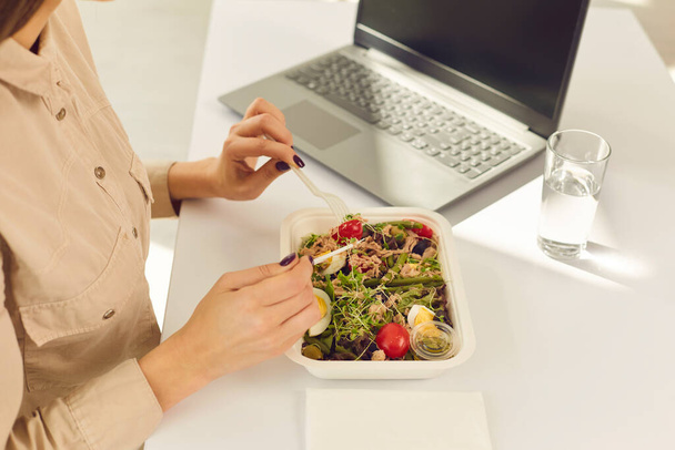 ノートパソコンと水でデスクに座って健康的な箱入り食品の注文を楽しんでいる女性のオフィスワーカー - 写真・画像