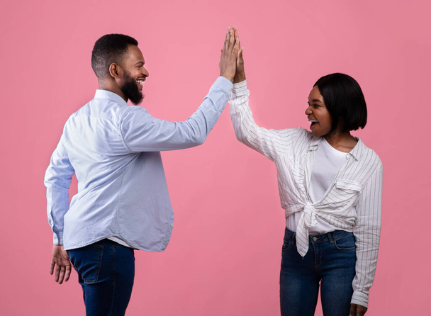 Ομαδική εργασία και συνεργασία. Μαύρο ζευγάρι δίνει κόλλα πέντε ο ένας στον άλλο, γιορτάζοντας την κοινή επιτυχία σε ροζ φόντο - Φωτογραφία, εικόνα