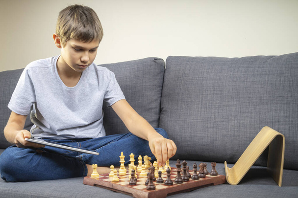 Подросток учится играть в шахматы онлайн с планшетным компьютером. Онлайн-образование, дистанционное обучение, развлечения на дому - Фото, изображение