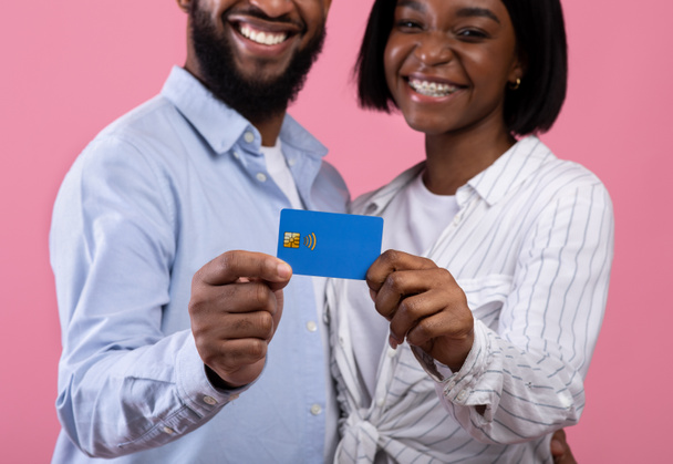 Pembe stüdyo arka planında kredi kartı tutan siyah evli çiftin görüntüsü, ellerine odaklan. - Fotoğraf, Görsel